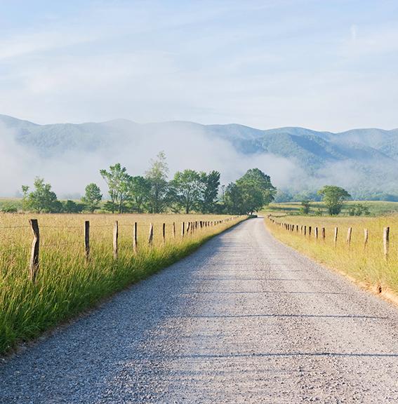Gravel road running through fields in Tennessee with a mountain ridge in the background