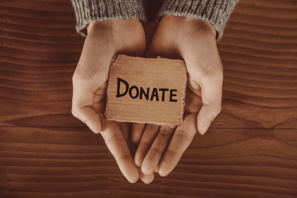 Hands holding a small sign reading "Donate"