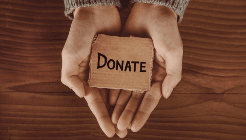 Hands holding a small sign reading "Donate"