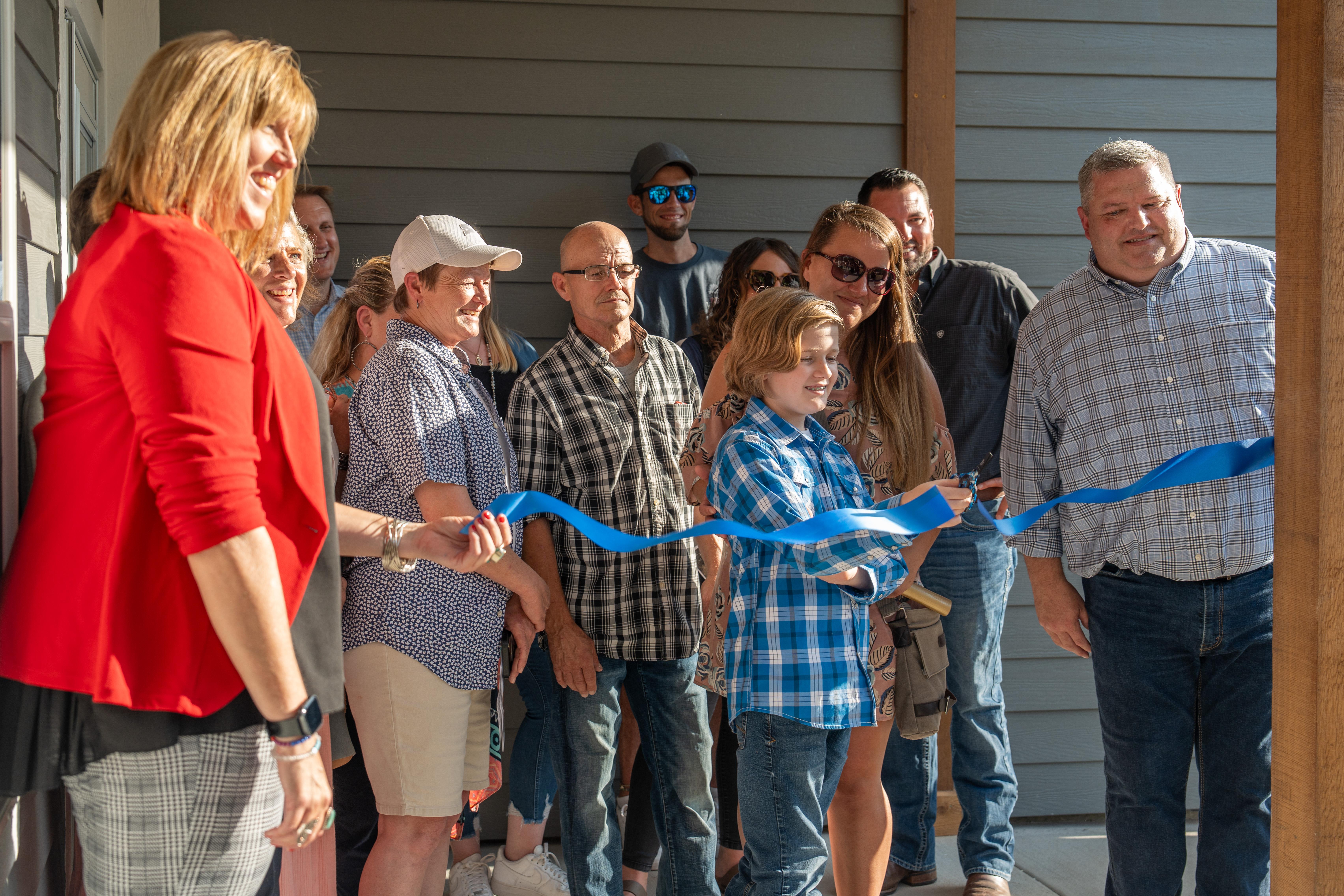 A group of people cutting a blue ribbon for a new home