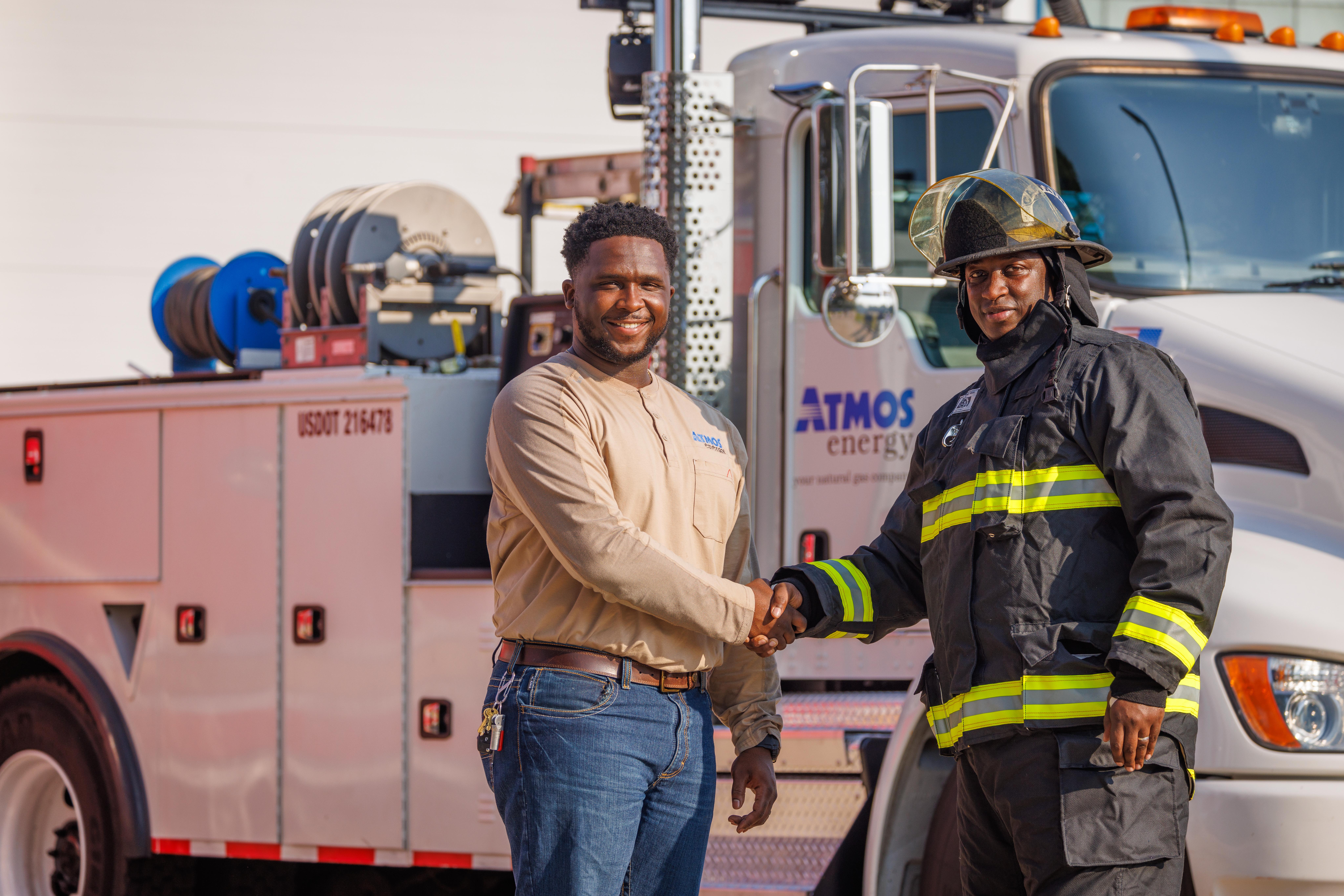 Two men shaking hands. The man on the right is a firefighter and they're standing in front of an Atmos Energy service truck.