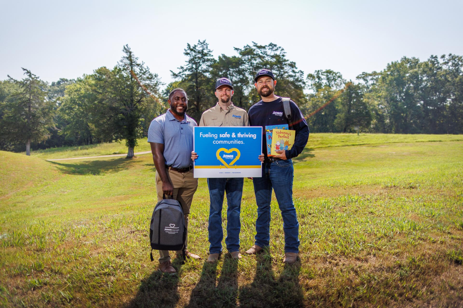 Atmos Energy employees standing in a green field holding a sign that says fueling safe and thriving communities